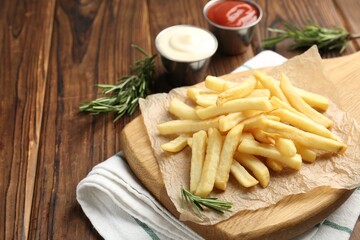 Tasty french fries served with sauces and rosemary on wooden table, closeup. Space for text