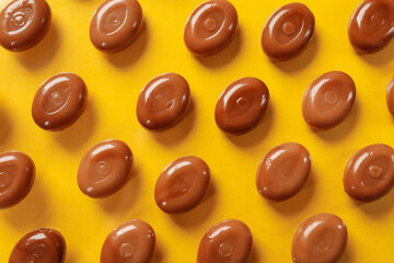Many tasty caramel candies on yellow background, flat lay