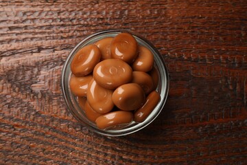 Many tasty caramel candies on wooden table, top view