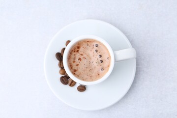 Aromatic coffee in cup, beans and saucer on light table, top view