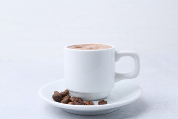 Aromatic coffee in cup, beans and saucer on light table, closeup