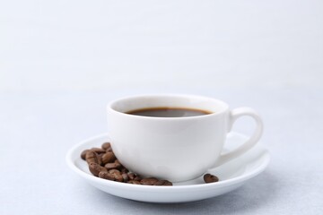 Aromatic coffee in cup, beans and saucer on light table, closeup