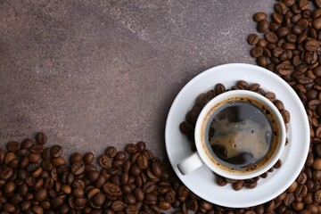 Aromatic coffee in cup, saucer and beans on brown textured table, flat lay. Space for text