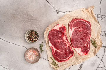 Raw fresh beef steak on a paper with spices on a gray background. Top view with copy space. High...