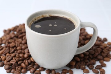 Aromatic coffee in cup and beans on white background, closeup
