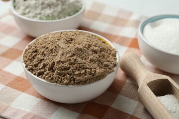 Different types of flour in bowls and scoop on table, closeup