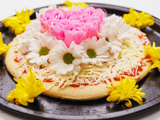 Pink roses in heart love shape and white chamomile flowers on top of a pizza and on dark metal...