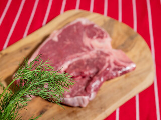 Fresh uncooked T bone steak with fresh dill and garlic cloves on wooden cutting board and on classic red and white stripe table cloth. High quality beef meat product. Butcher craft.