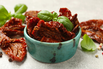 Delicious sun dried tomatoes in bowl and spices on gray textured table, closeup
