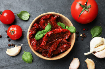 Tasty sun dried tomatoes, fresh vegetables and peppercorns on black table, flat lay