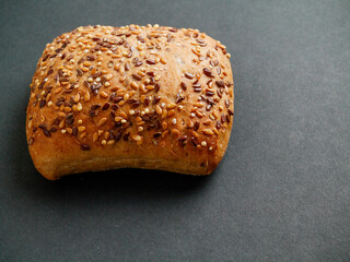 One small roll with grain and seeds on dark background. Fine bakery product made from high quality premium ingredients, Small taste crusty bread.