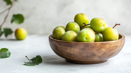 A rustic bowl brimming with ripe green greengage plums on a white surface, evoking a summer harvest