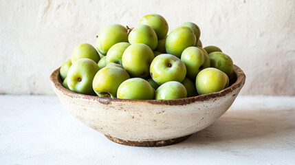 A rustic bowl brimming with ripe green greengage plums on a white surface, evoking a summer harvest