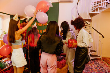 Group of six friends standing and holding balloons and gifts