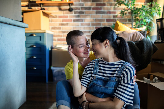 Young female lesbian couple hugging and sitting on the floor of of a new apartment they just moved in