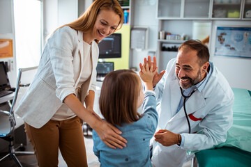 Smiling doctor using stethoscope to check young girl at medical clinic with mother nearby