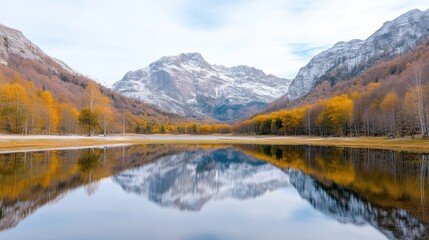 Fototapeta premium Autumnal mountain lake reflecting snow-capped peaks. Tranquil scene of serene water mirroring fall foliage and mountains