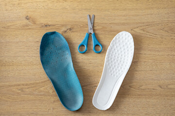 Top view of blue and white insoles with scissors on wooden floor, representing choice and customization for comfortable athletic footwear support