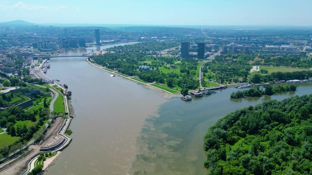 Aerial view of Belgrade where the Sava and Danube rivers meet. Visible landmarks include Kalemegdan Fortress (Beogradska tvrđava), city bridges, and U&scaron;će Park &mdash; a perfect urban-meets-nature panorama
