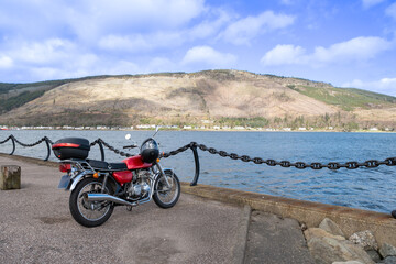 motorbike freedom in Scotland countryside. Bike parked at Holy Loch Dunoon on sunny day. Adventure outdoors travel lifestyle for solo traveler on motorcycle transportation tour in the great outdoors