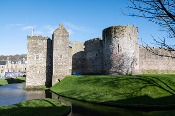 Rothesay Castle ruin and moat on the Scottish island of Bute with stone circular plan towers and curtain walls on sunny summer blue sky day