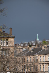 rooftop skyline of Glasgow tenement residential accommodation with prominent religious building green copper cross against dark cloudy sky