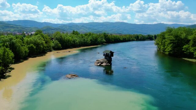 Aerial view of Bajina Ba&scaron;ta and the iconic Kućica na Drini (Drina River House), peacefully perched on a rock in the middle of the emerald Drina River, surrounded by lush nature and mountain landscapes