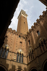 Upward view of The Torre del Mangia in Siena, Italy, framed by the Palazzo Pubblico's brick walls.