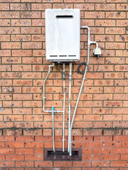 Photograph of an old and relatively small electrically powered hot water system that is mounted on an external brick wall of an office building.
