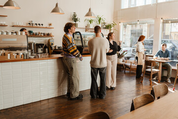 A female owner stands and talks while two male customers and a female employee stand next to her, in a cafe