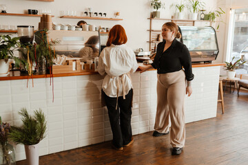 A female owner and a female employee are standing at a bar with a male employee behind it, in a cafe