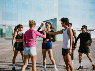 A group of six athletes laugh and talk while about to give each other a high five, outdoors