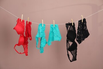 Women's underwear. Beautiful panties and bras on clothes line against light brown background