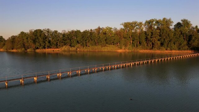 Luftaufnahme der 260 m langen befahrbaren Holzbruecke zur Mausinsel im Woerthsee, Bayern. Die private Insel ist dicht bewaldet und liegt ruhig im Landschaftsschutzgebiet bei Inning am Ammersee. 