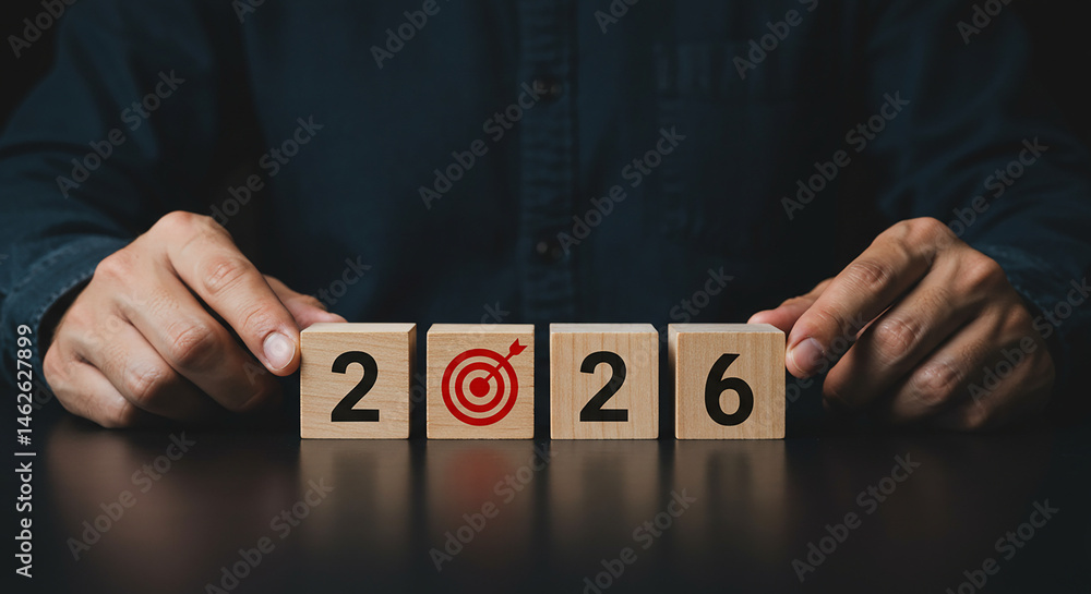 Poster man setting wooden blocks with the year and a target symbol on a dark surface for the year ahead rea