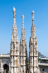 Fototapeta premium The intricate rooftops of the Duomo in Milan showcase remarkable Gothic architecture, featuring beautifully detailed spires that reach for the sky against a bright blue backdrop.