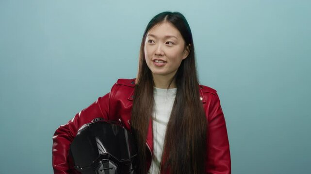Woman in red jacket holding helmet against blue background looking thoughtful and confident in studio lighting with a refreshing appeal