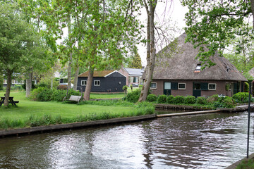 Obraz premium Giethoorn, Netherlands – A picturesque village with canals and rustic thatched-roof houses in a scenic farm area on a warm spring day in Europe.