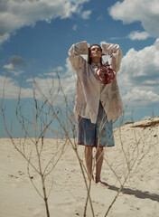 Fashion shooting in the desert, girl model in a beige shirt and blue shorts.