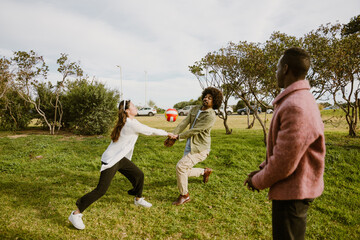 A man stands and watches as his male and female friends standing next to him catch a ball, outdoors
