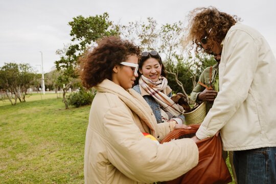 Group of four friends standing and smiling while looking at a bag one of them is holding, outdoors