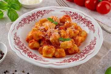 Traditional potato gnocchi with tomato sauce, parmesan cheese and fresh basil on a plate on a concrete background. Italian cuisine. Top view, copy space.