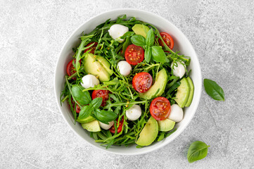Fresh salad with arugula, mozzarella, tomatoes and avocado in a bowl. Healthy vegetarian dish.