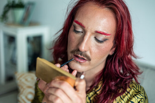 Young non-binary person applying lipstick at home