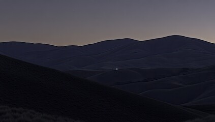Silhouette of rolling hills at twilight. A single light source is visible in the distance