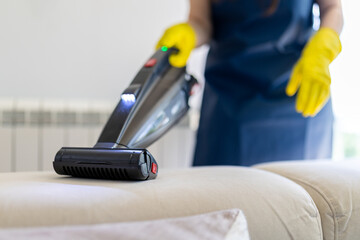 Cleaning upholstery with a handheld vacuum while wearing rubber gloves for a tidy home environment
