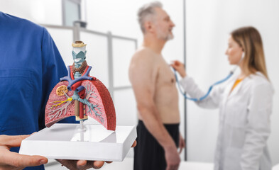 Obraz premium Doctors assess lung health of senior patient using anatomical model of lungs during diagnosis and auscultation lungs of patient to determine treatment options