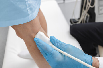 Close-up of vascular sensor of ultrasound machine during the process of examining a sick leg for varicose veins with vascular scientist