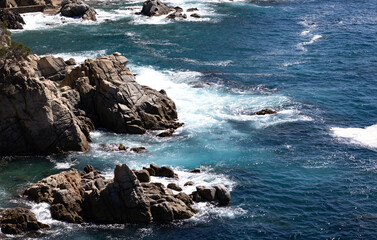 Waves gently washing over rugged coastal rocks in clear turquoise and deep blue ocean waters 