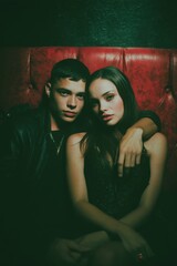A young couple, lost in intimacy, share a tender moment while seated on a red velvet sofa.